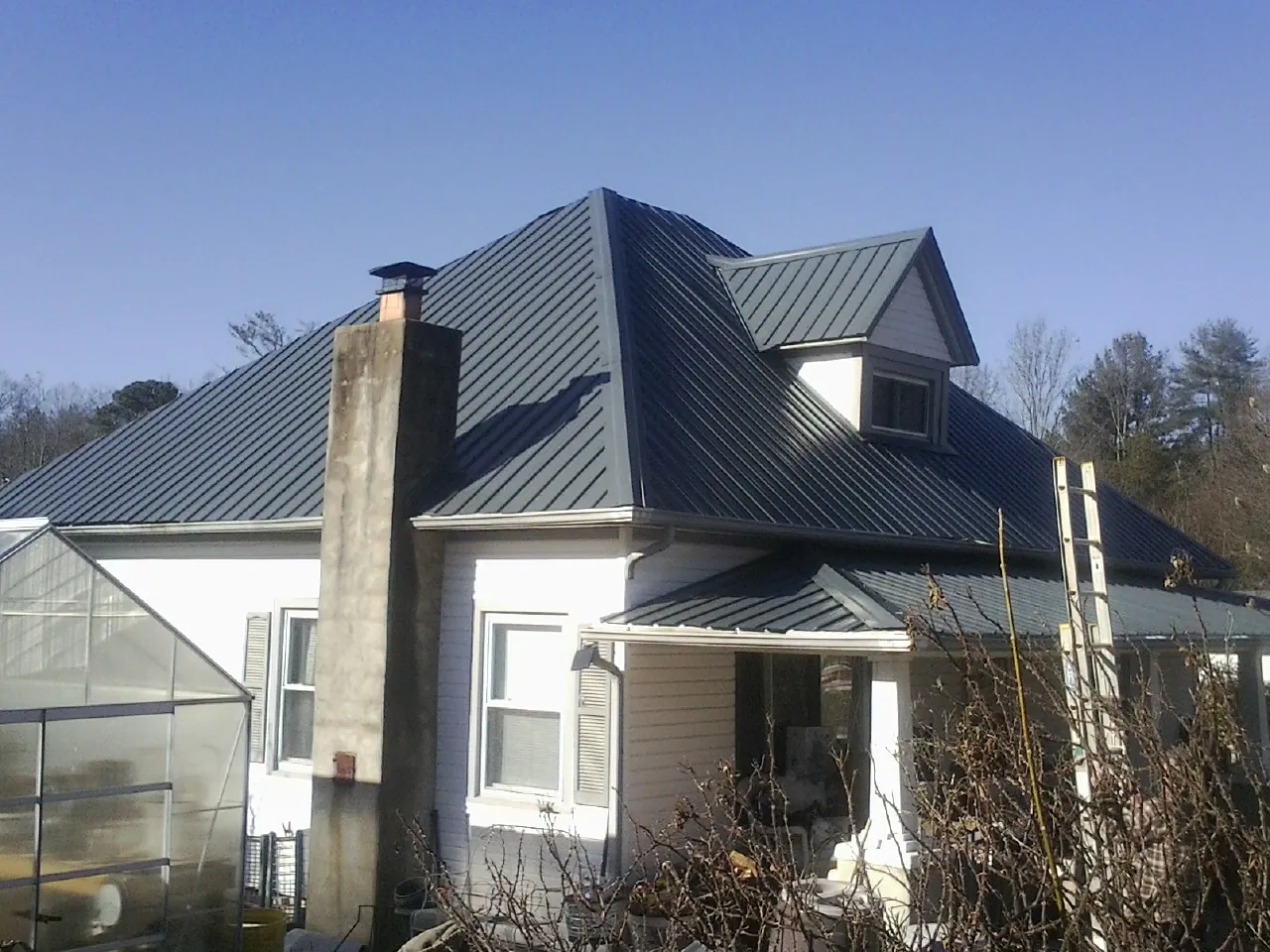 Dark blue standing seam metal roof on a white farmhouse with dormer — Slate & Tile Roof Repair by Roofing Brothers in Delaplane