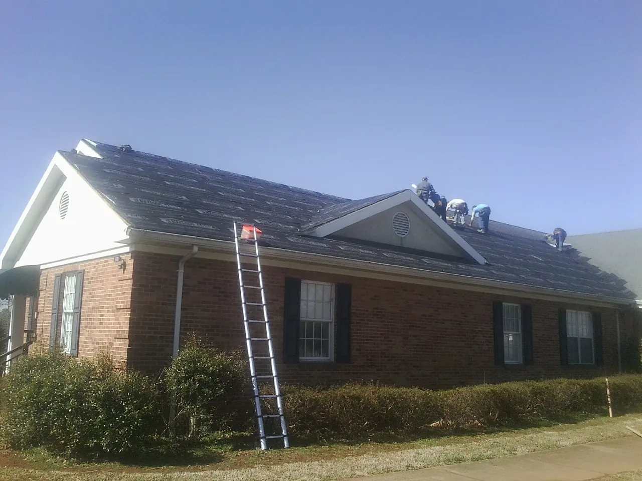 Crew tearing shingles off a brick ranch roof with a ladder set — Emergency Roof Repair work by our crew in Delaplane