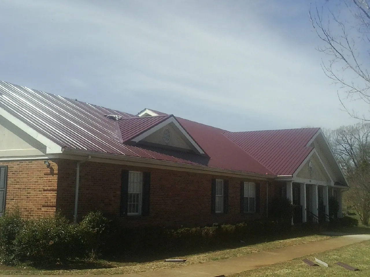 Red metal roof with gabled entries on a long brick building, from a Hail Damage Roof Repair job in Delaplane