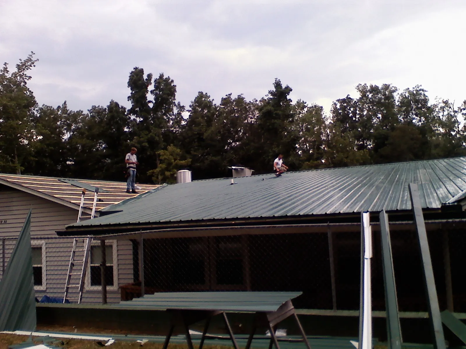 Two roofers installing green metal panels above a covered porch in Delaplane