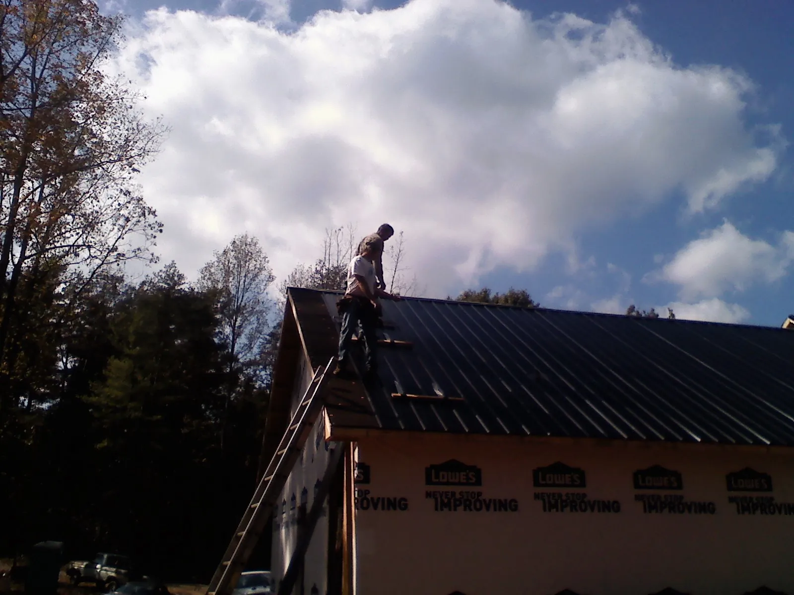 Roofer fastening dark metal panels high against a cloudy sky, from a Roof Inspection job in Delaplane