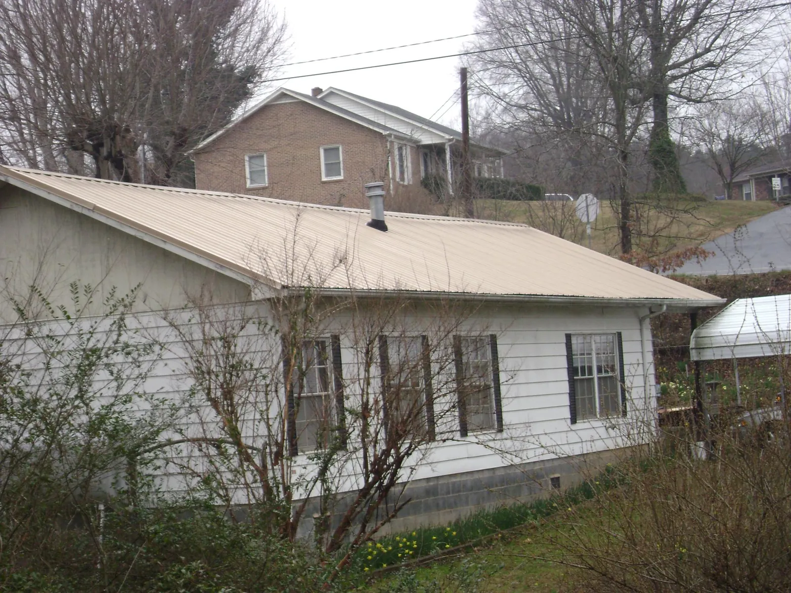 Tan metal roof on a white sided house set into a hillside — Commercial Roofing by Roofing Brothers in Delaplane